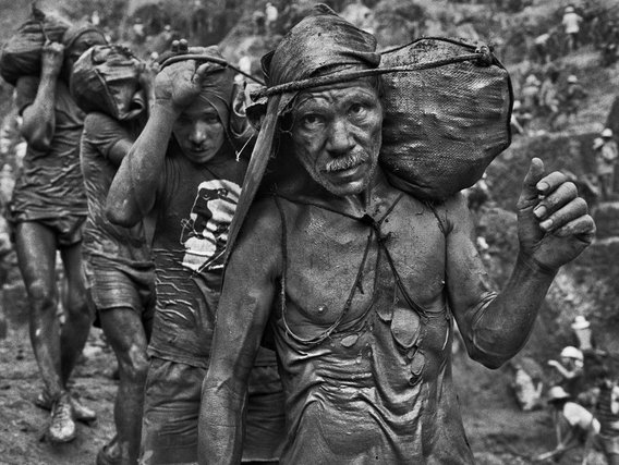 Miners Mineiros carregados com sacos caminham por uma trilha.